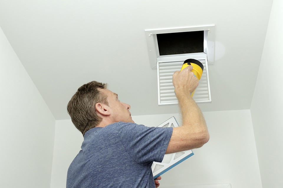 HVAC specialist inspecting interior ductwork with tools to identify heavy dust accumulation